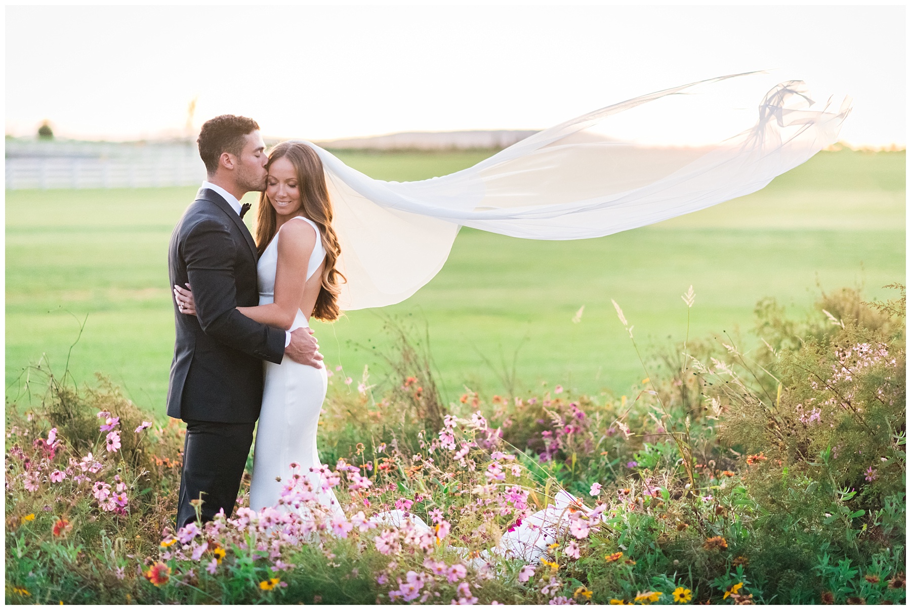 Groom kissing the bride’s forehead during a Bluebird Manor wedding in a wildflower field
