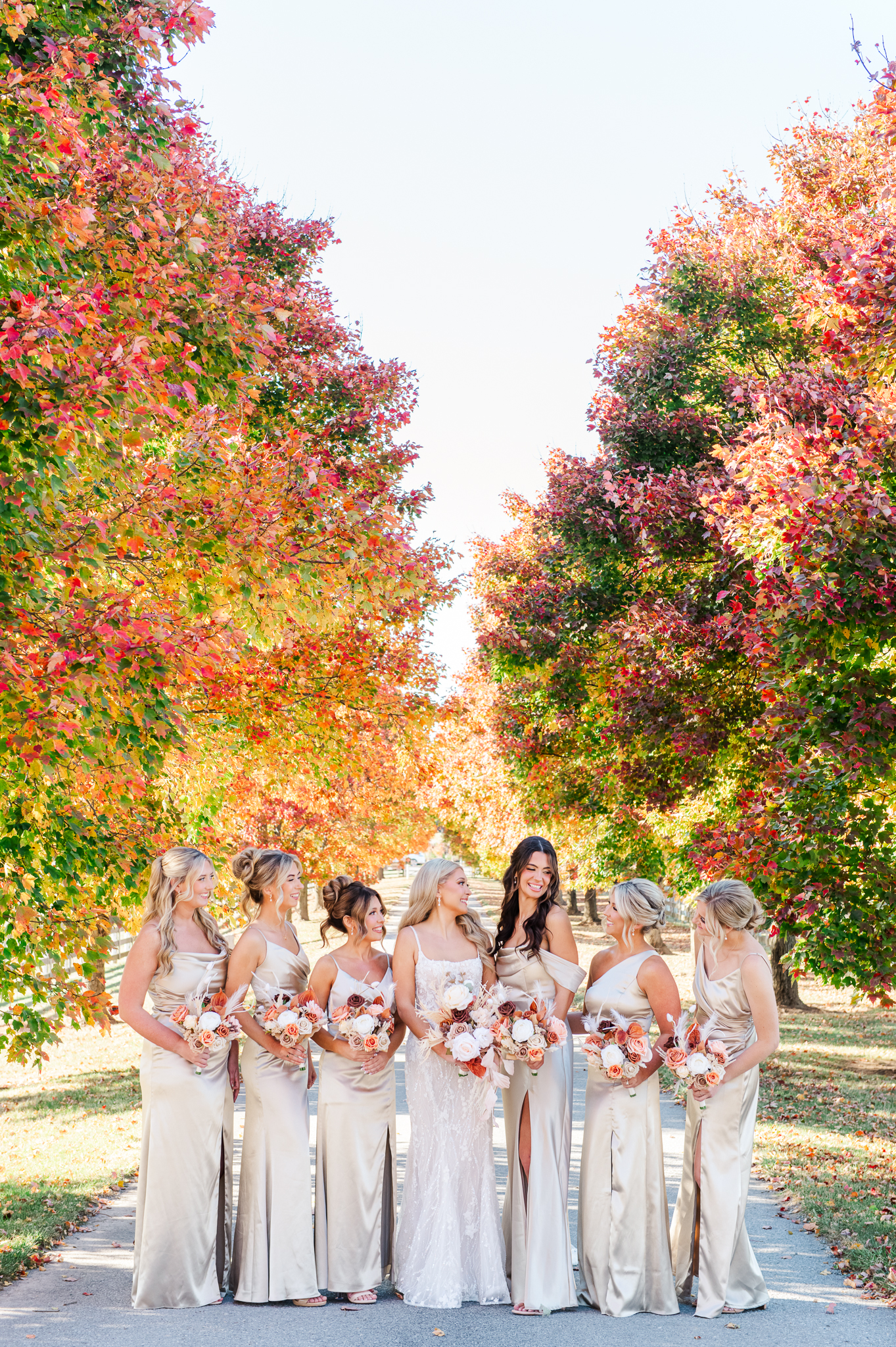 Bride with bridesmaids beneath the iconic fall foliage at Bluebird Manor wedding venue.