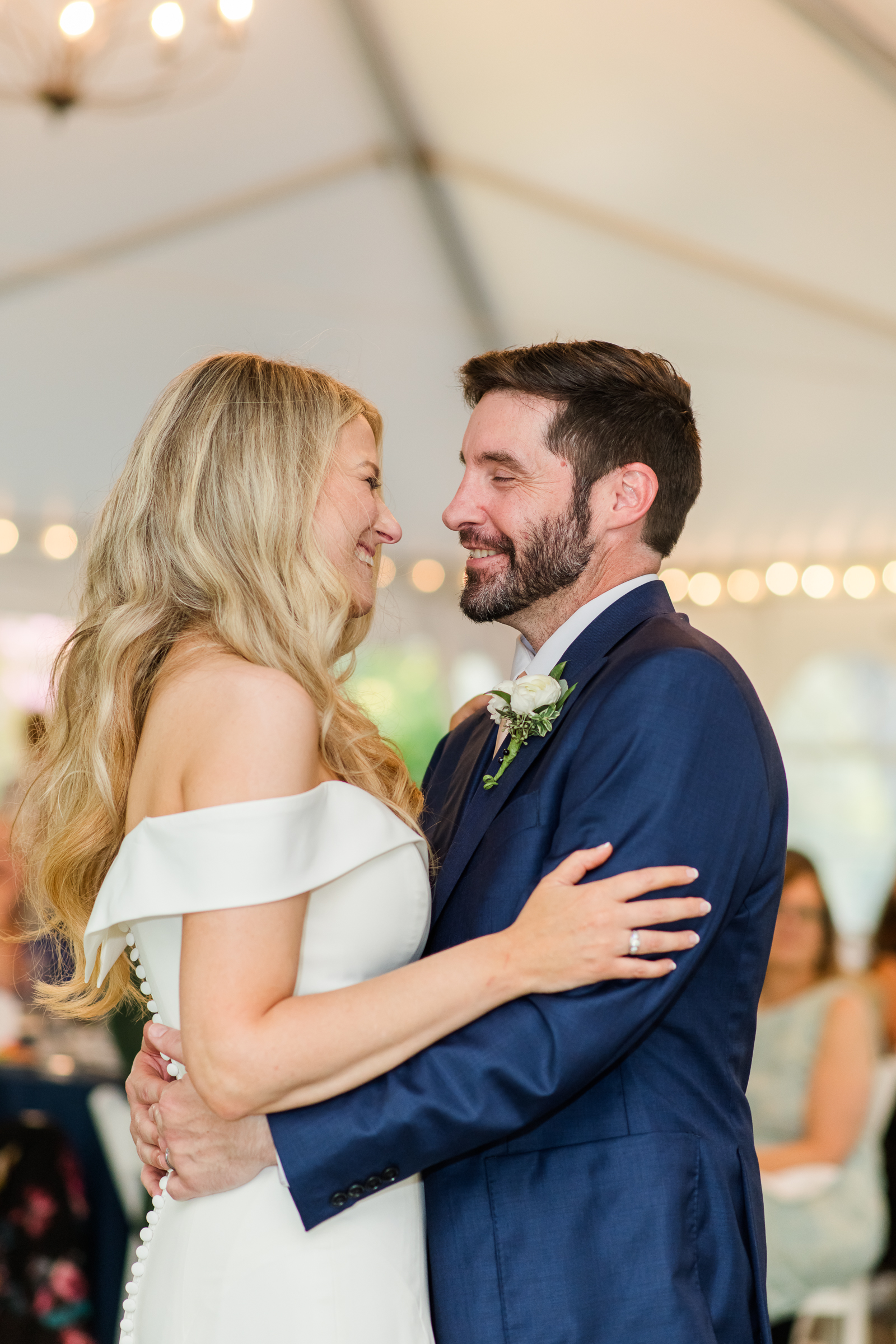 A sweet bride and groom first dance inside a lit white tent reception.