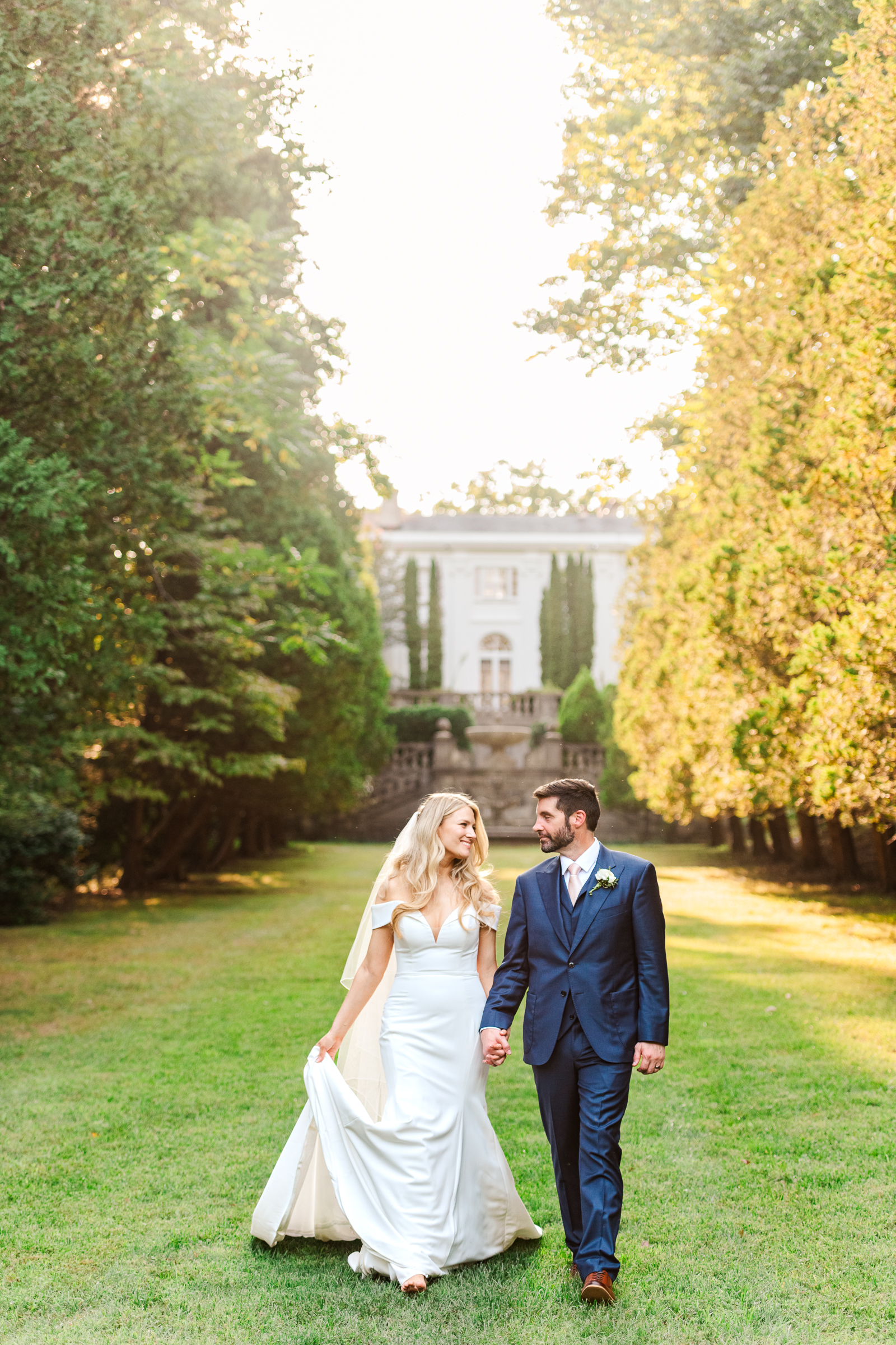 A bride and groom take a romantic stroll through formal gardens of Strong Mansion during a sunset portrait session by Mary Sarah Photography.