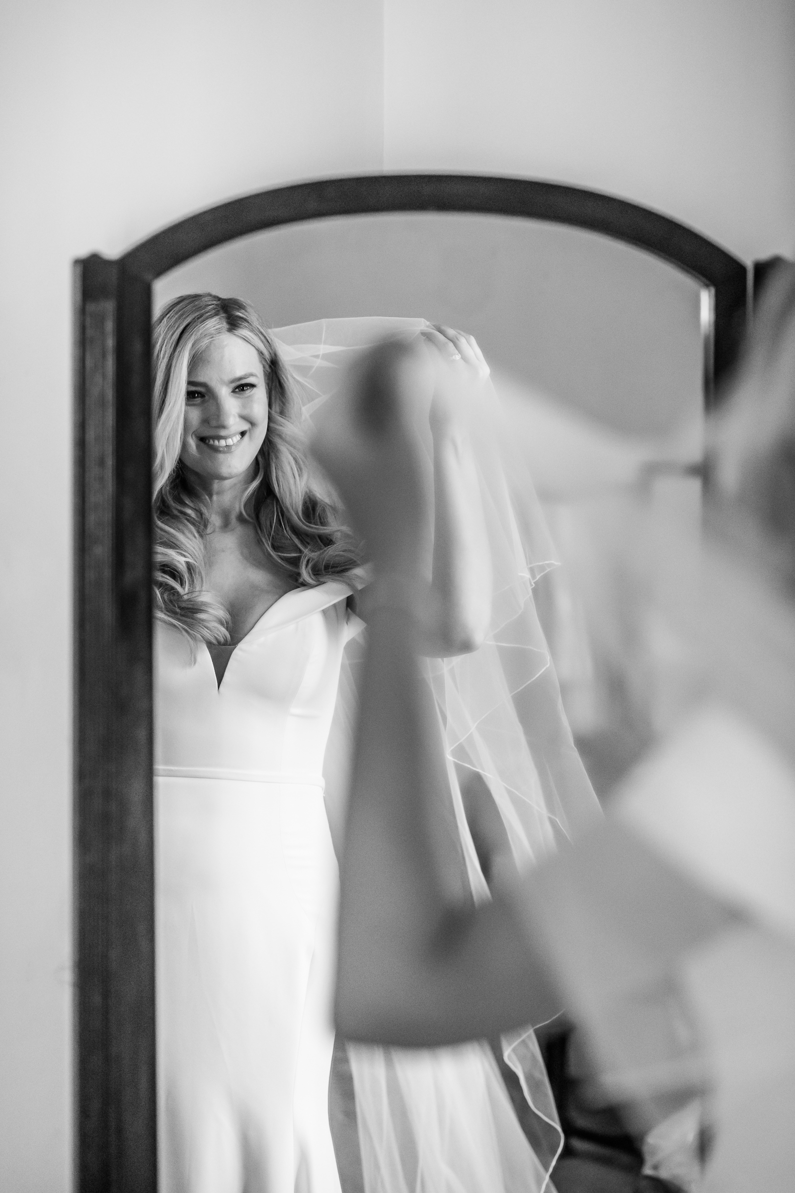 A stunning black and white portrait of a bride lifting her veil while looking into a mirror at Strong Mansion
