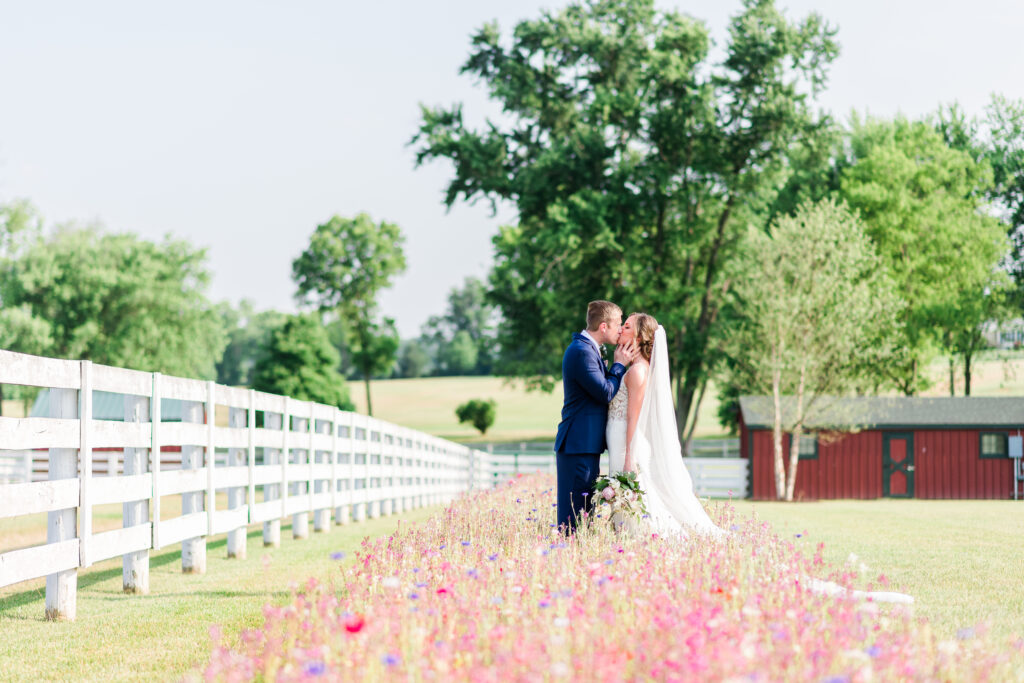 Bride and groom kissing in wildflower field at Bluebird Manor during summer wedding in Frederick Maryland