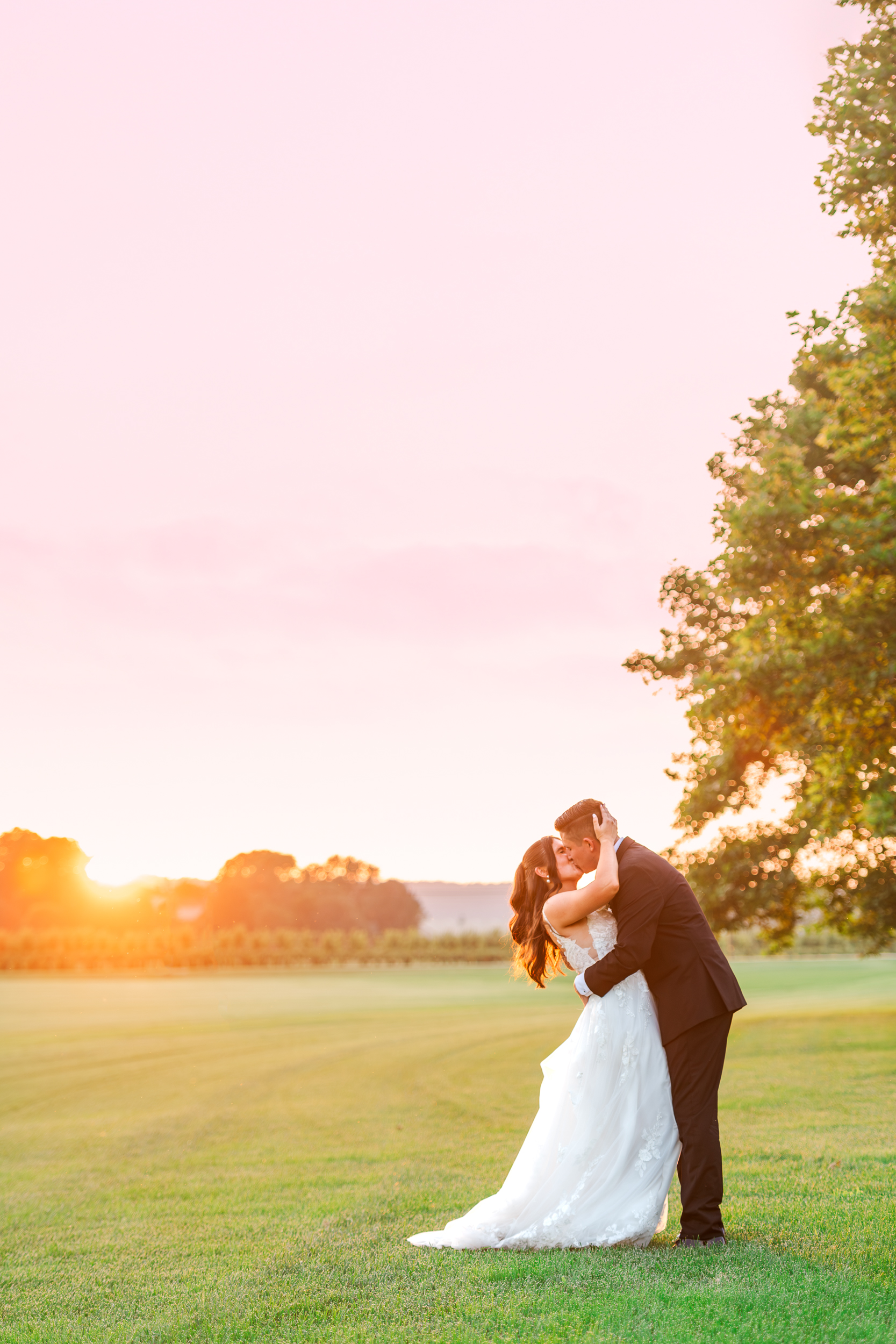 Bride and groom kiss with a pink sunset behind them