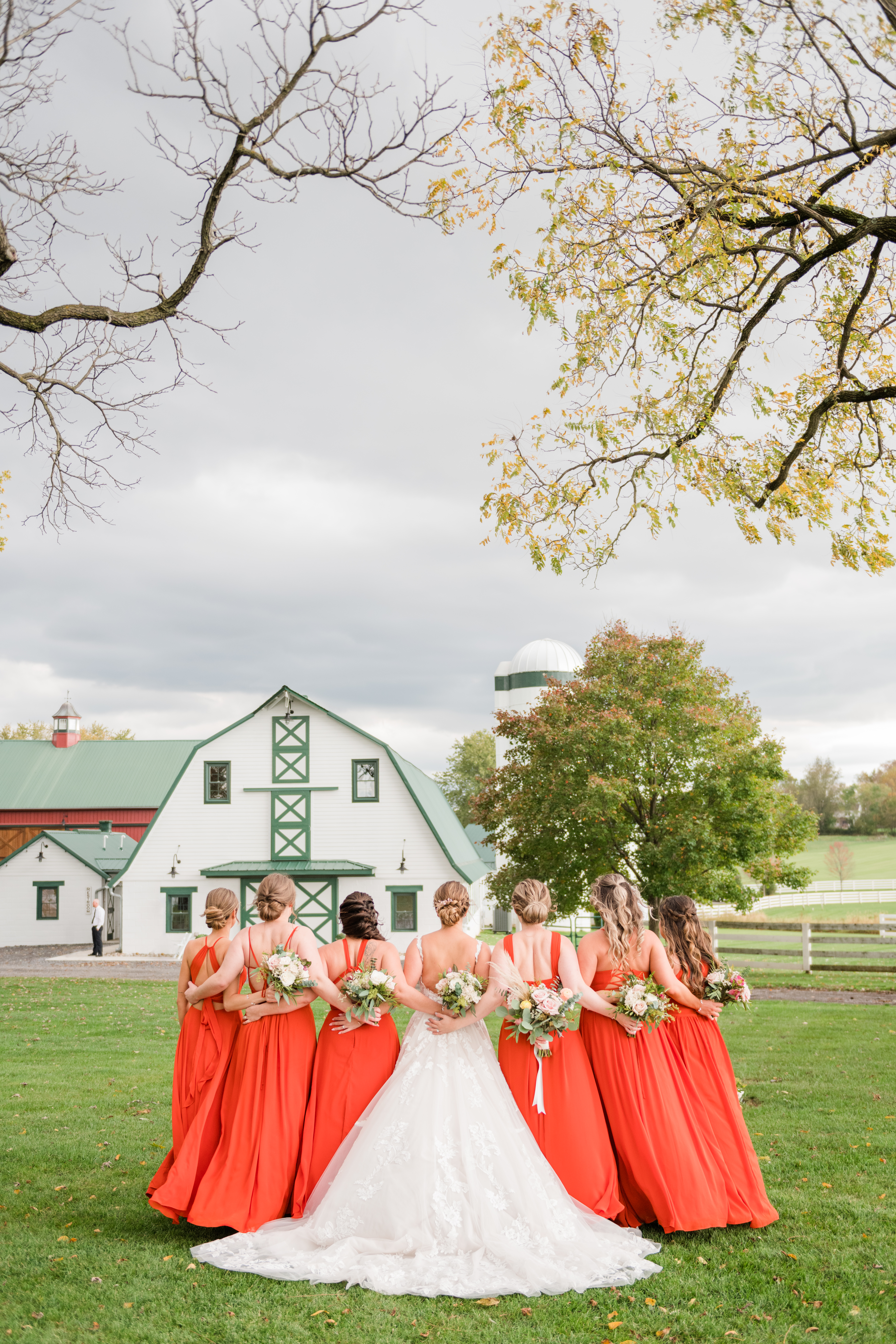 Bridal party in orange dresses standing in front of white barn at Bluebird Manor in Maryland