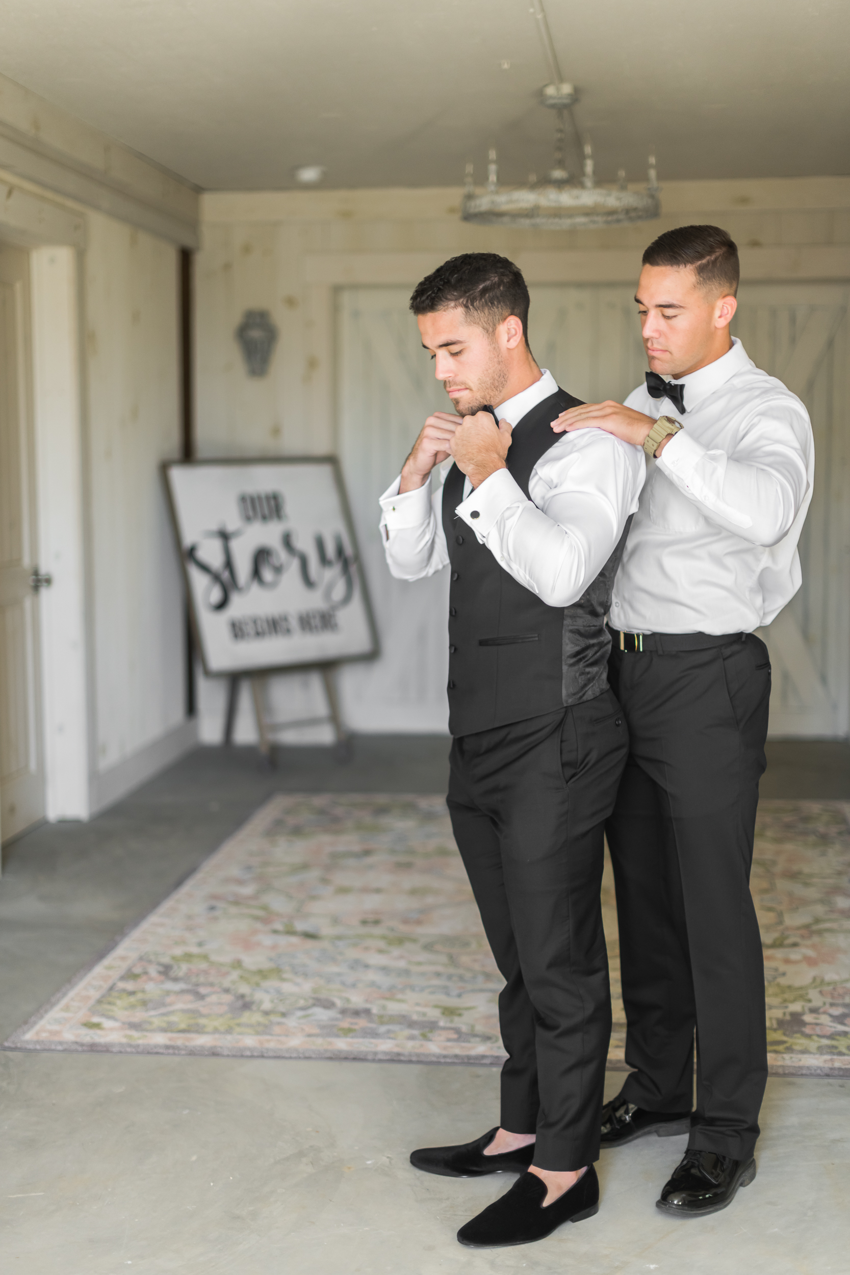 Groomsman helping groom adjust vest inside The Toolshed at Bluebird Manor