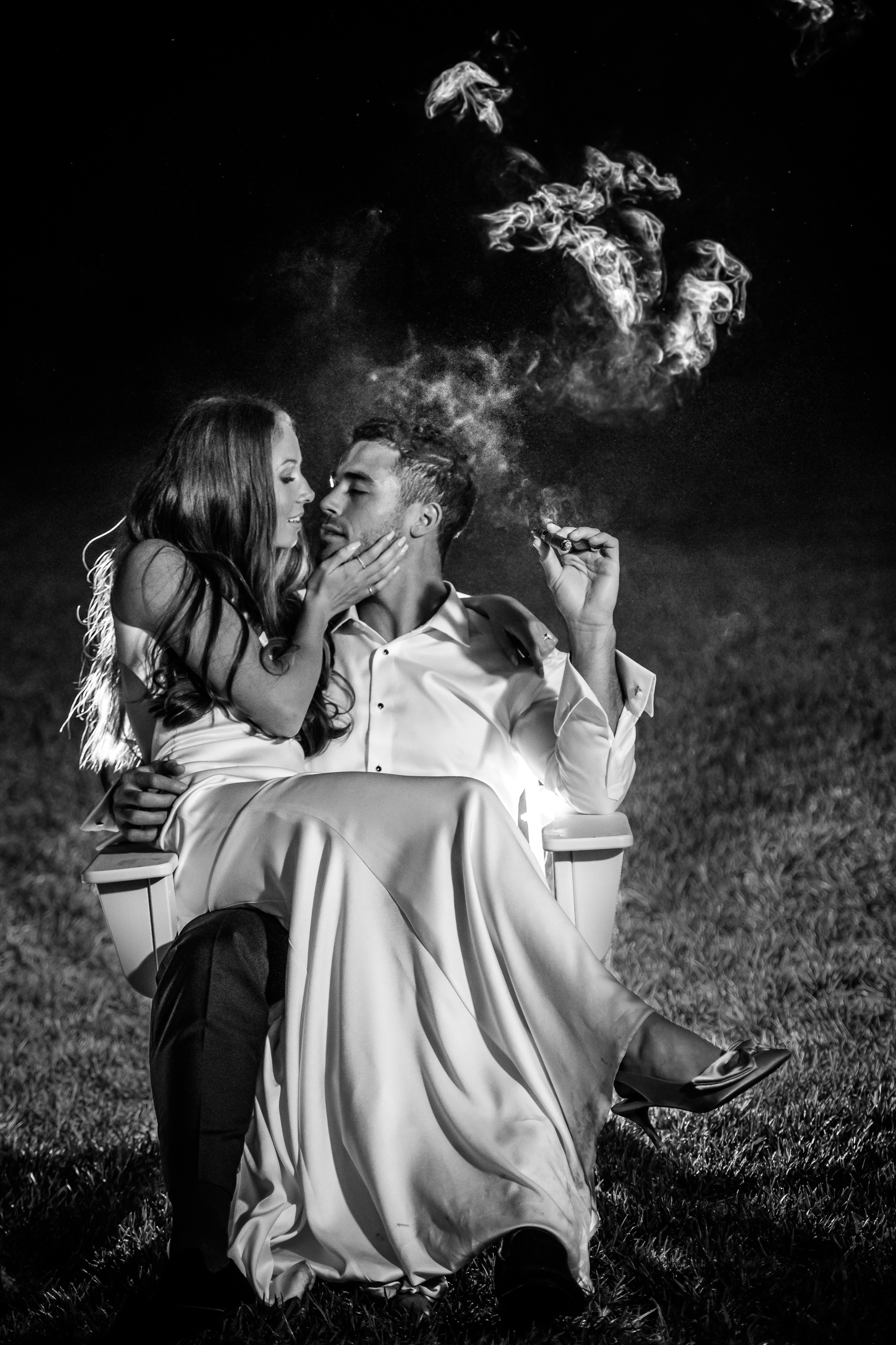 Black and white night portrait of bride and groom with groom holding a cigar and dramatic smoke.
