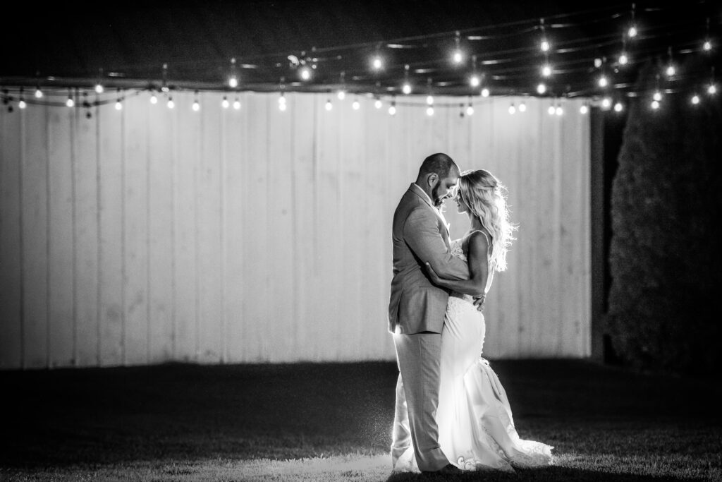 Bride and groom embracing under string lights at Bluebird Manor at night.
