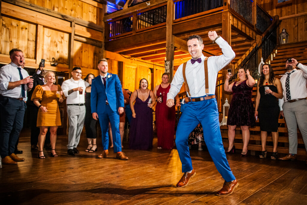 Groom dancing enthusiastically during wedding reception inside Bluebird Manor barn.