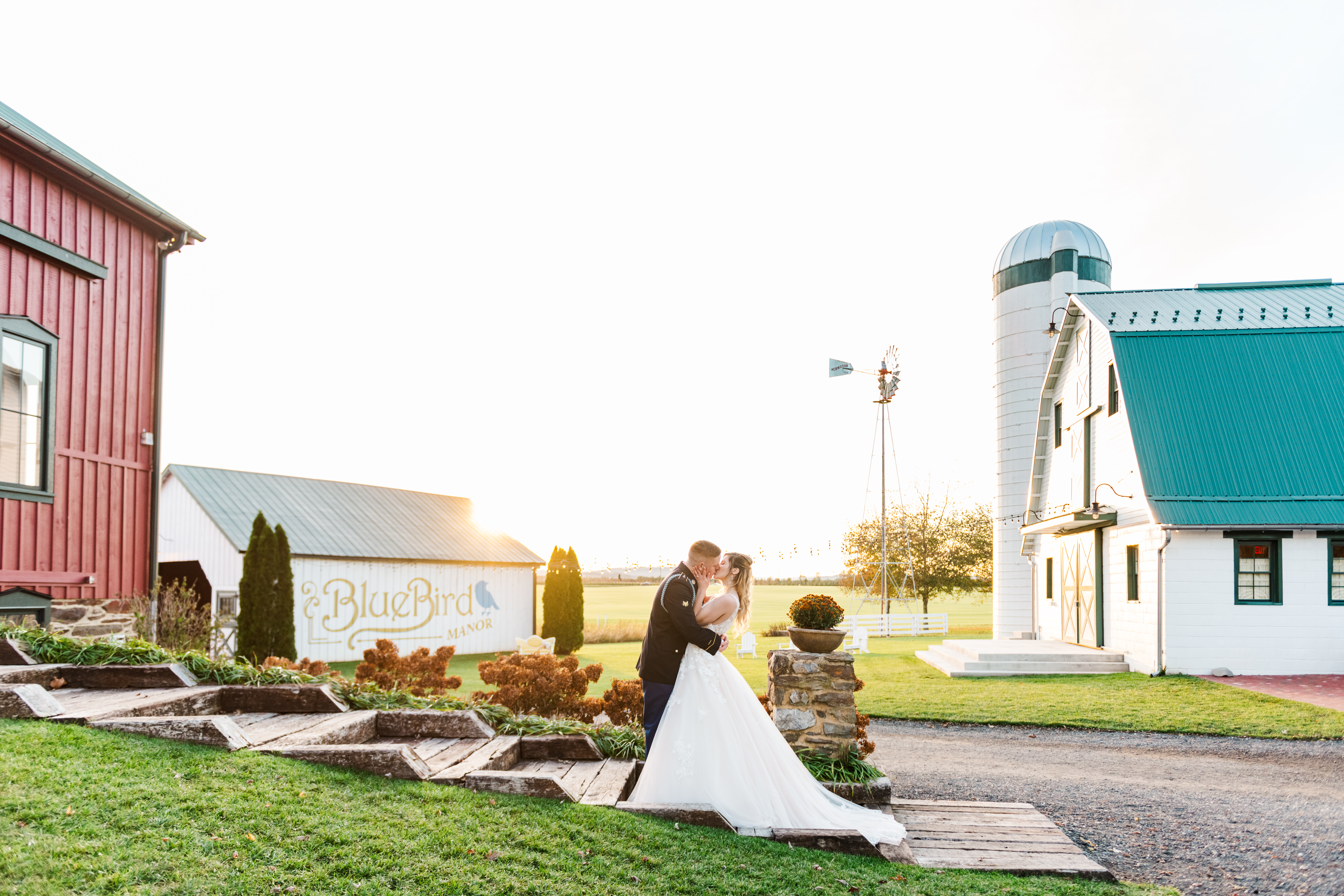 Bride and groom kissing on the steps of Bluebird Manor's reception with barns in background at sunset