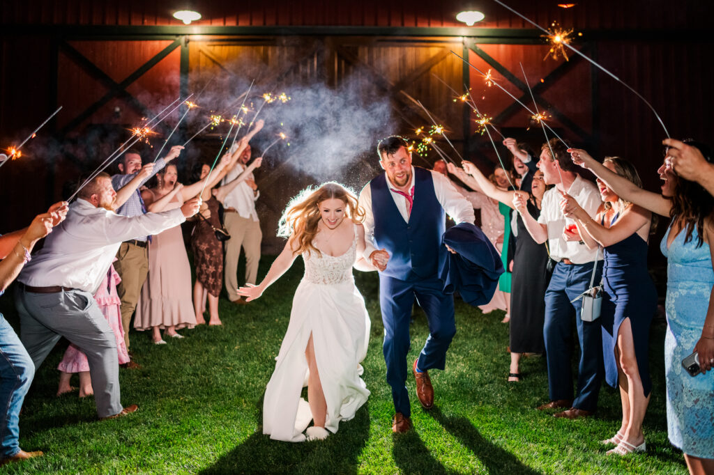 Bride and groom running through sparkler exit in front of Bluebird Manor barn.