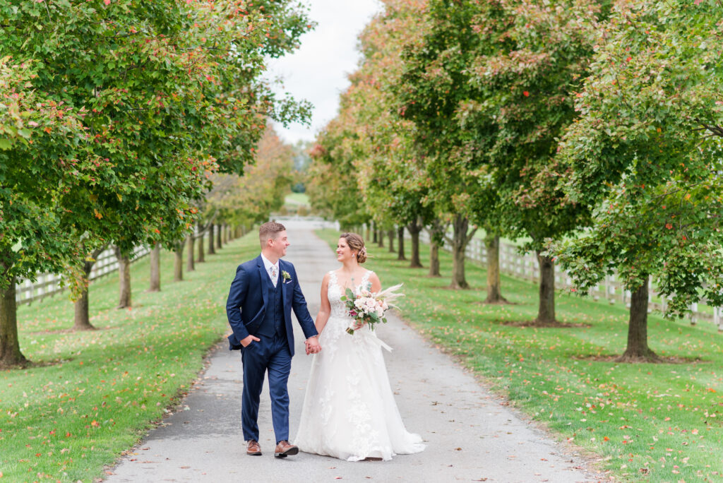 Bride and groom walking down tree-lined driveway at Bluebird Manor wedding venue