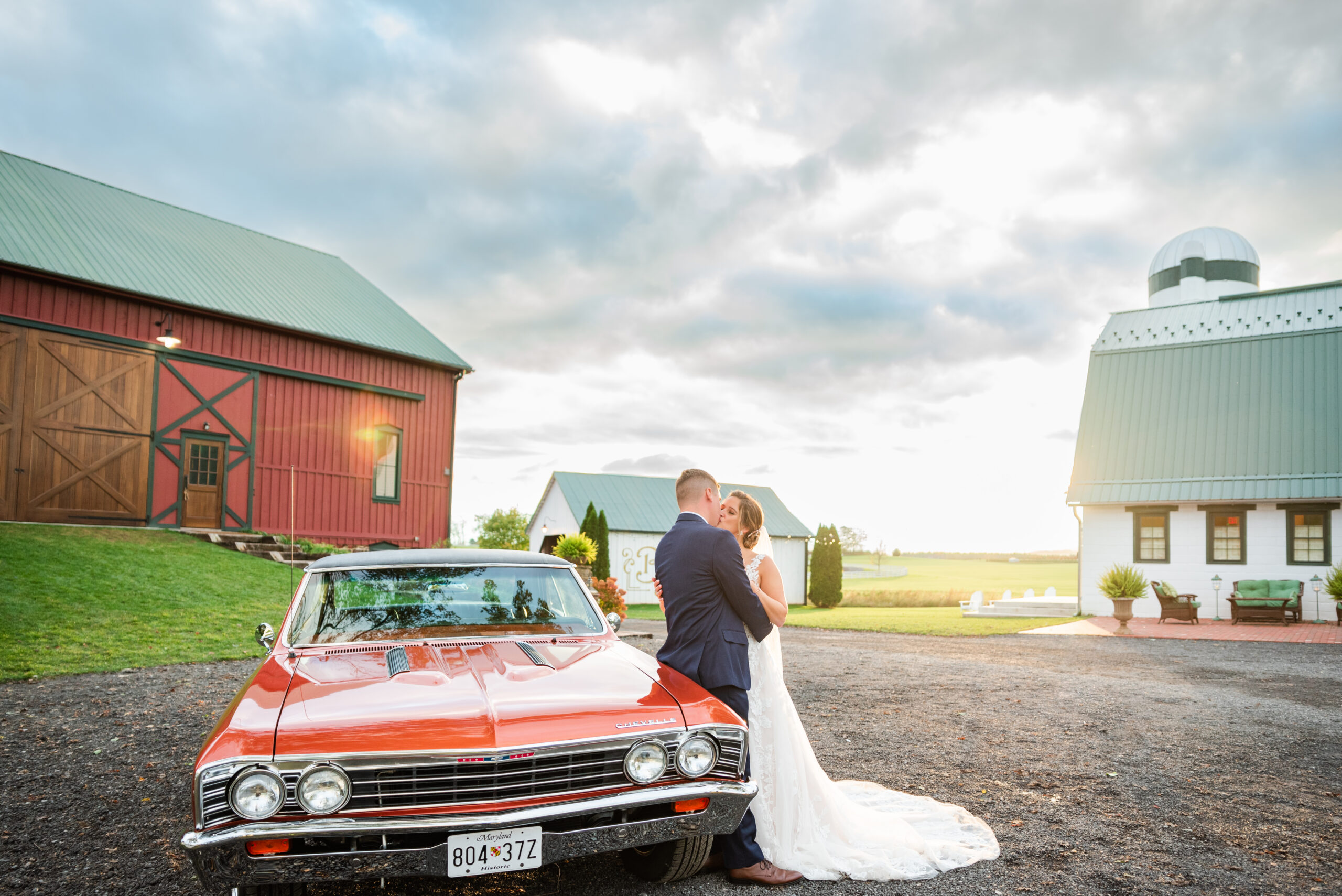 Bride and groom kissing beside vintage red car at Bluebird Manor wedding venue in Maryland