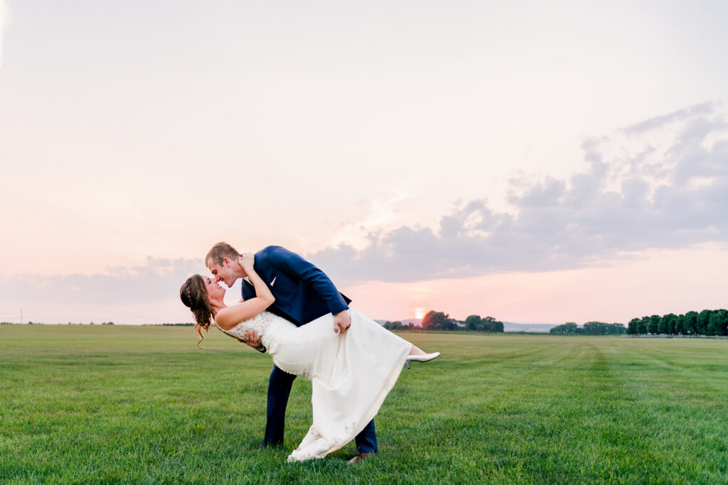 Bride and groom dipping kiss at sunset in open field at Bluebird Manor