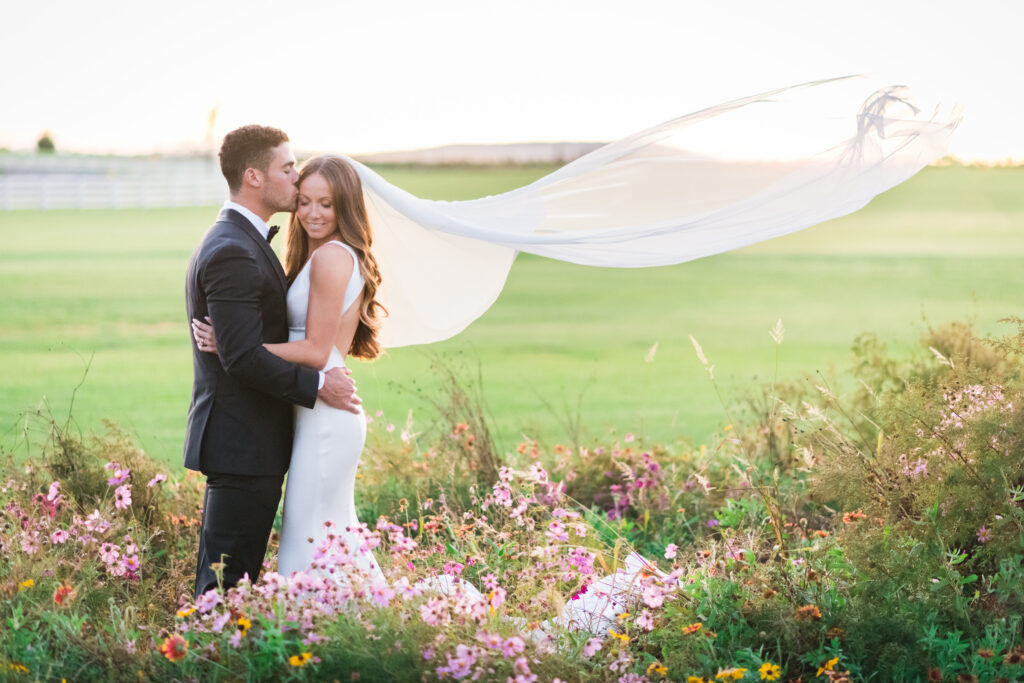 Bride and groom portrait in wildflower field with veil flowing 