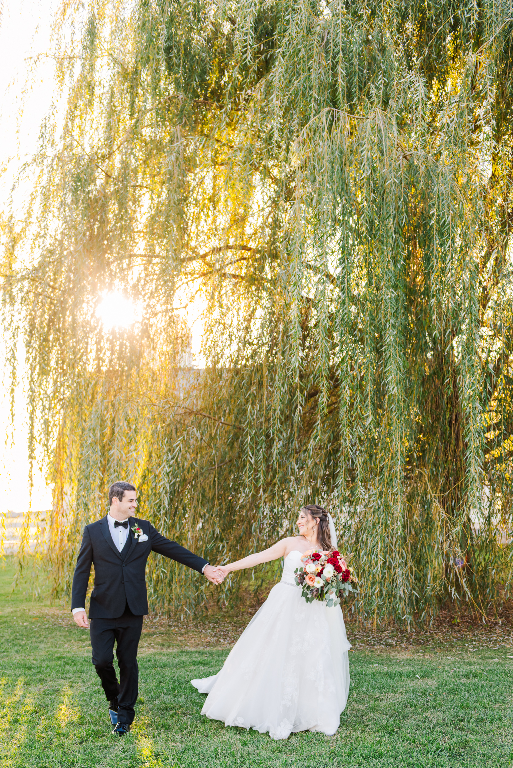 Bride and groom holding hands under willow tree at Bluebird Manor in Frederick County Maryland