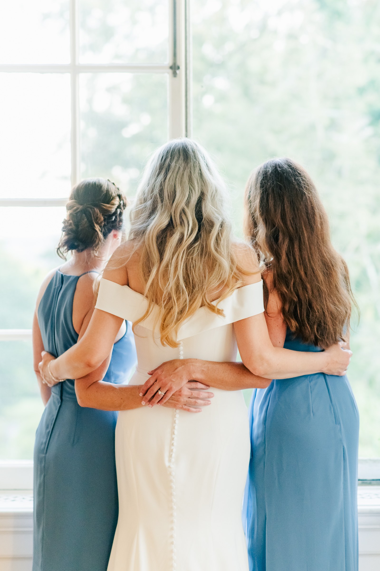 A sweet moment where the bride hugs her two closest bridsmaids from behind.