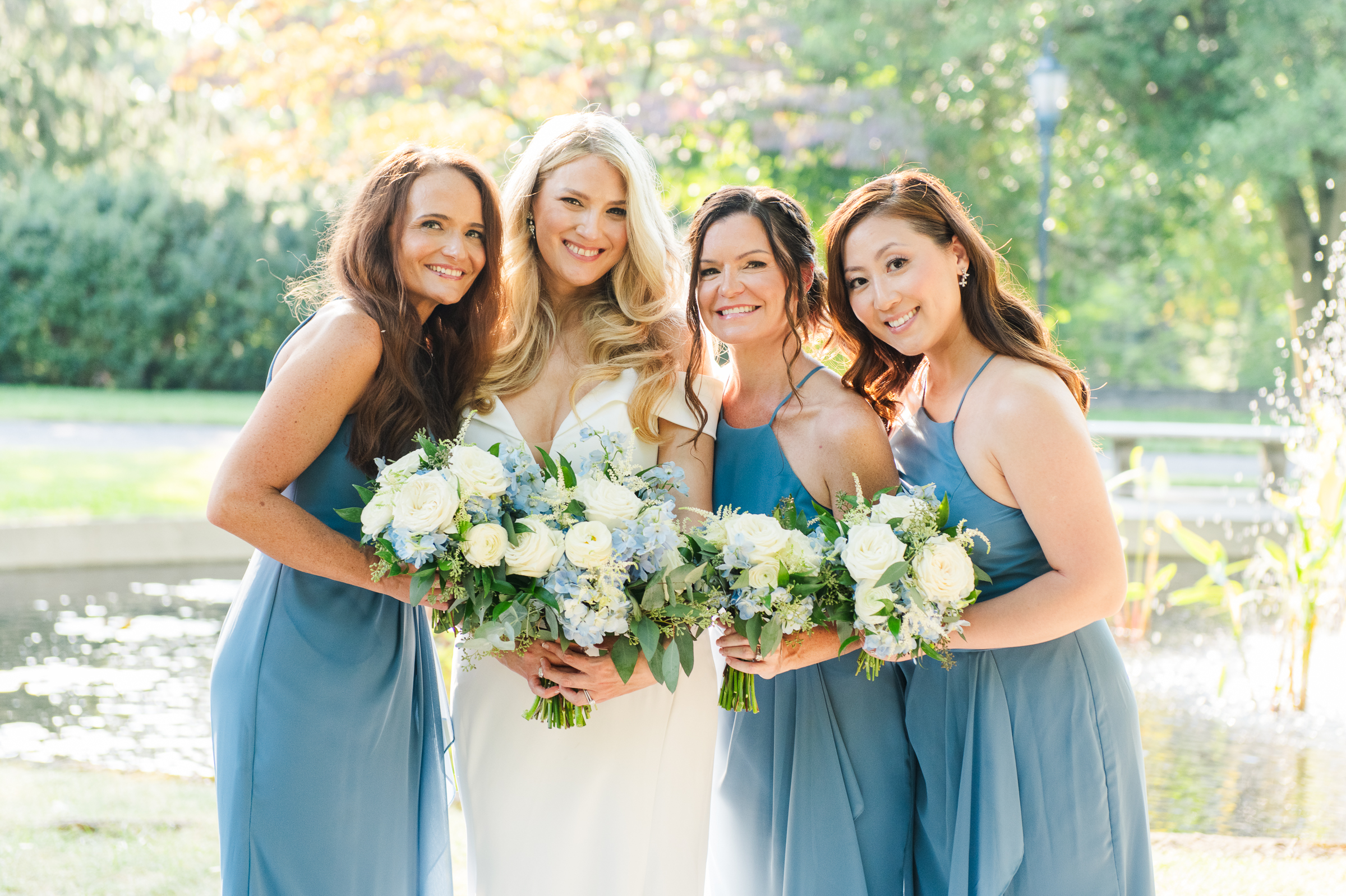 A bride hugging her bridesmaids in front of a pond