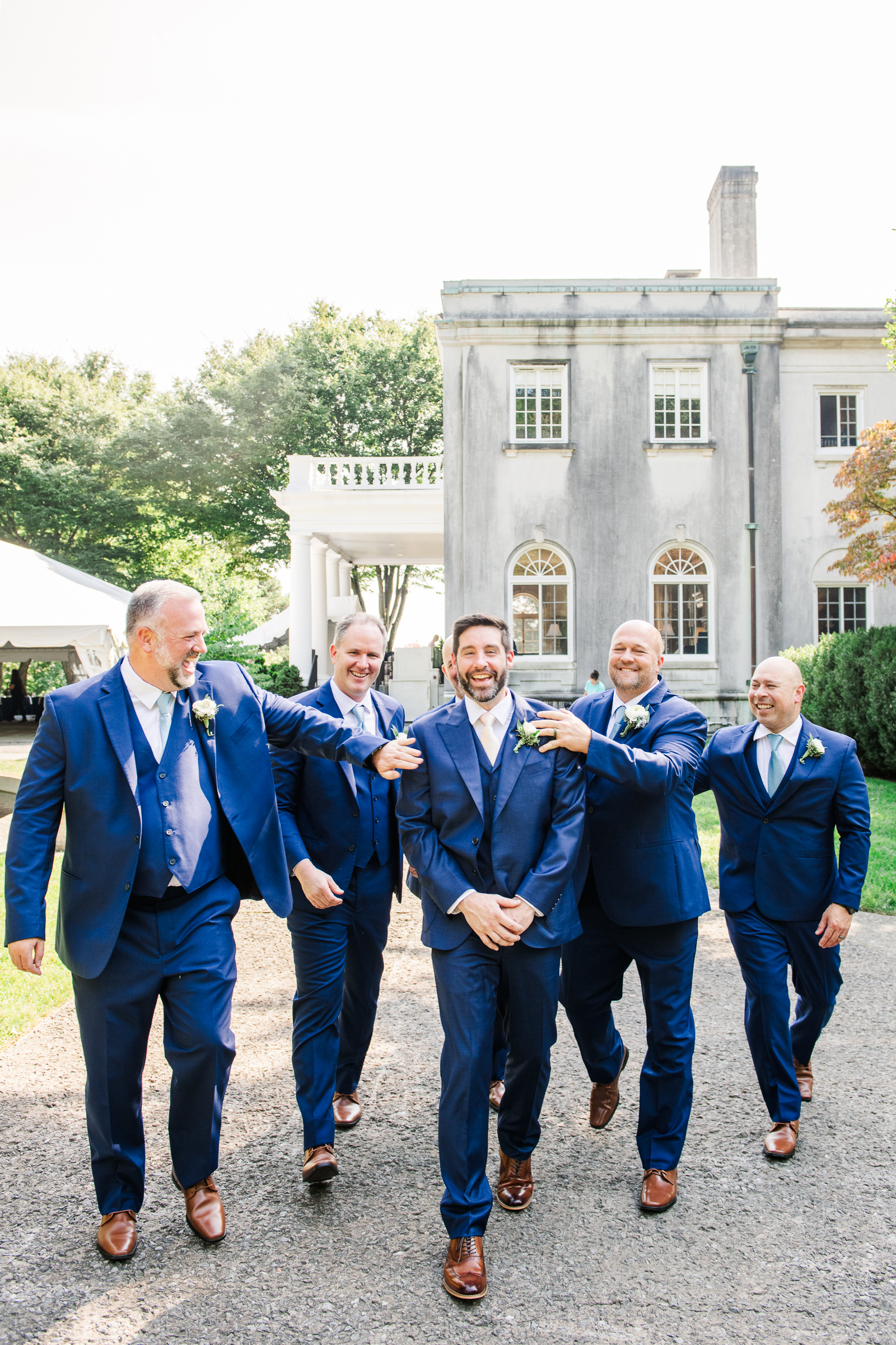 A candid pose of groomsmen laughing and walking together in front of the stunning Strong Mansion