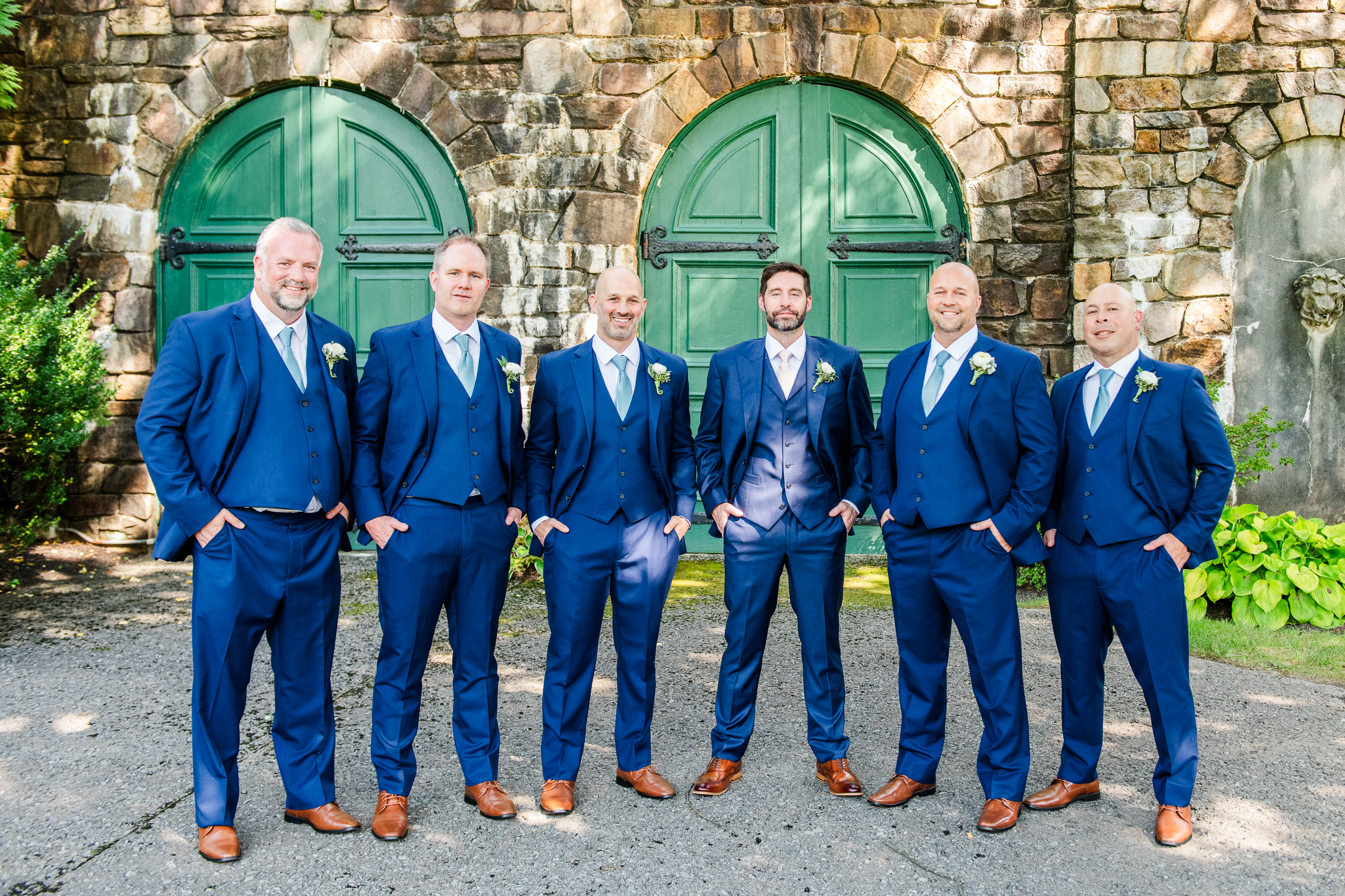 Groomsmen in navy blue suits against the classic stone architecture and green doors of Strong Mansion.