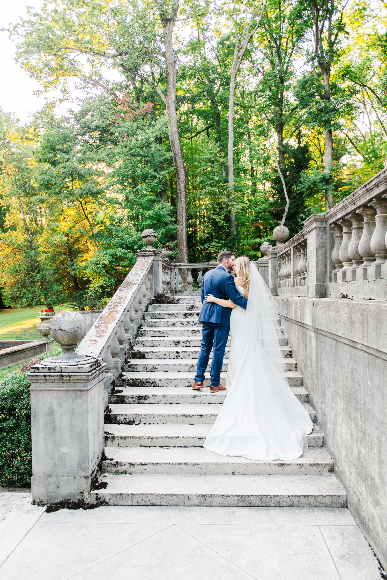 A bride and groom steal a kiss while walking up the stairs of the formal gardens of Strong Mansion during a sunset portrait session by Mary Sarah Photography.