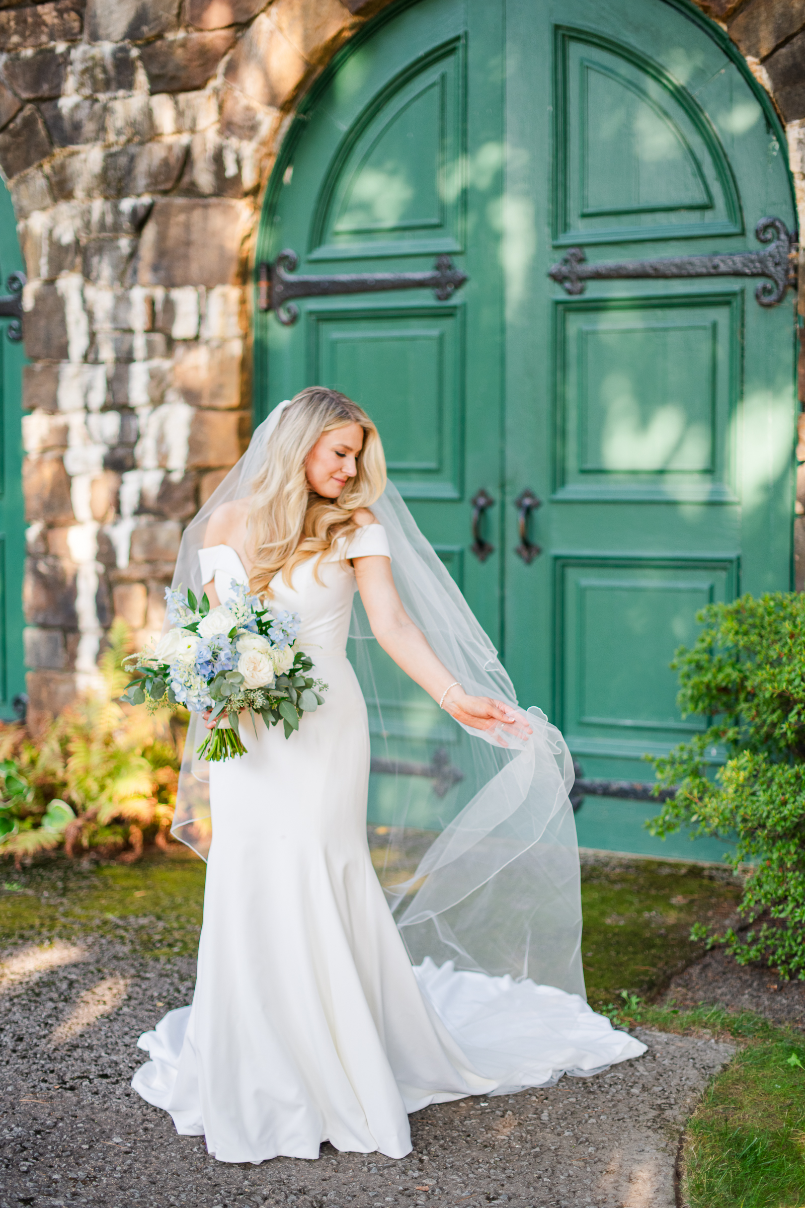 A stunning bridal portrait of a bride in a timeless gown posing against the classic stone architecture and green doors of Strong Mansion.